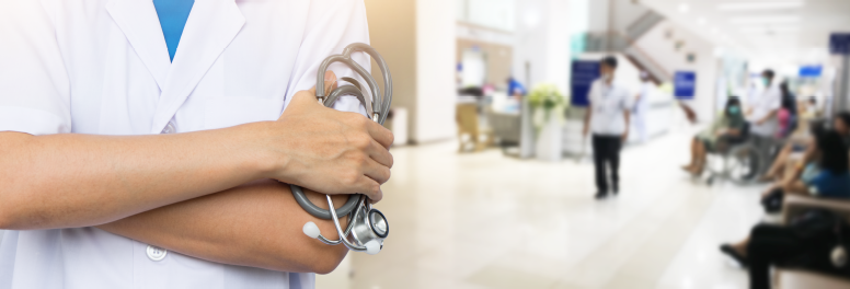 The torso of a doctor holding a stethoscope against a hospital setting with multiple patients and healthcare workers